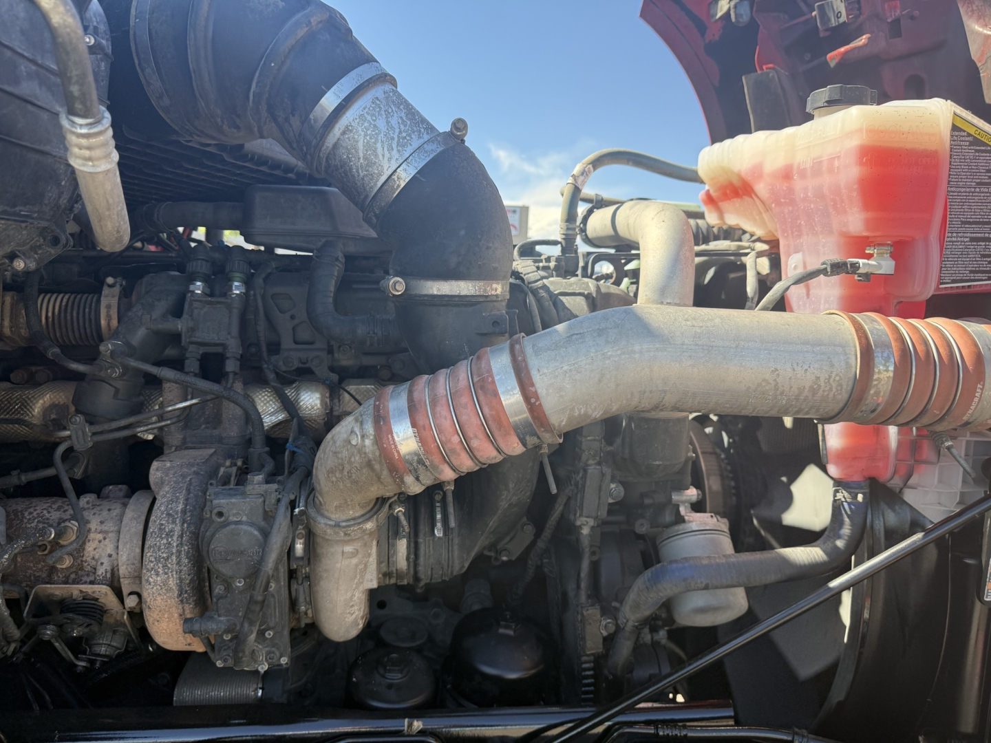 Kenworth T880 engine bay showing large metal intake piping and hoses, with coolant reservoir visible in the upper right.