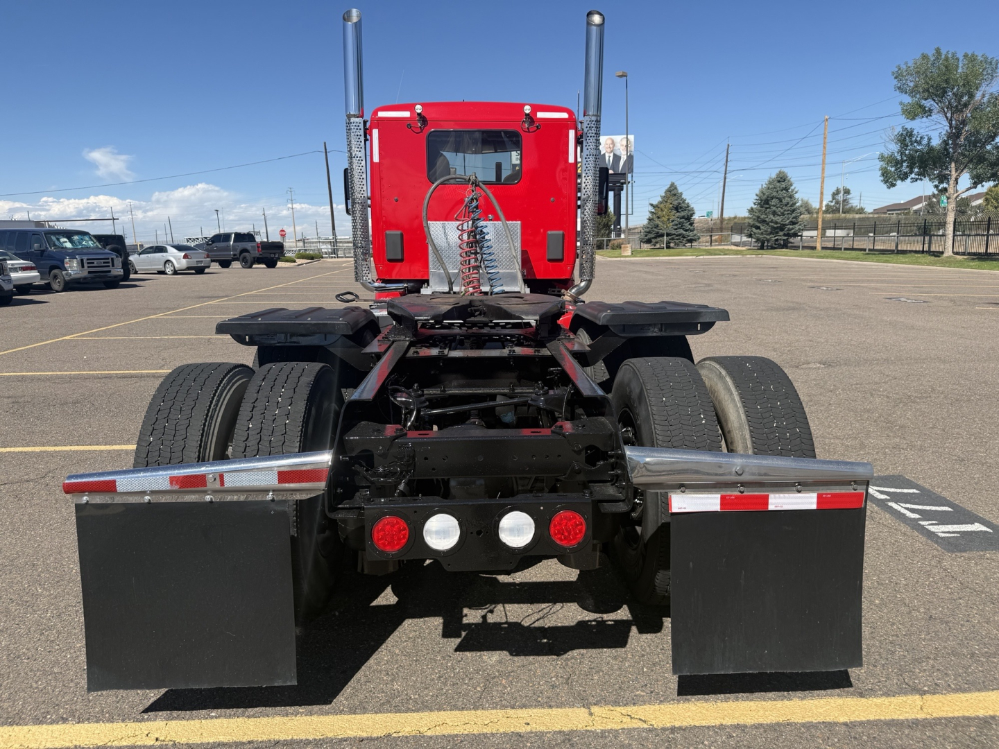 Kenworth truck rear view showing chassis and dual rear wheels, red sleeper cab, black mud flaps, and five rear lights.