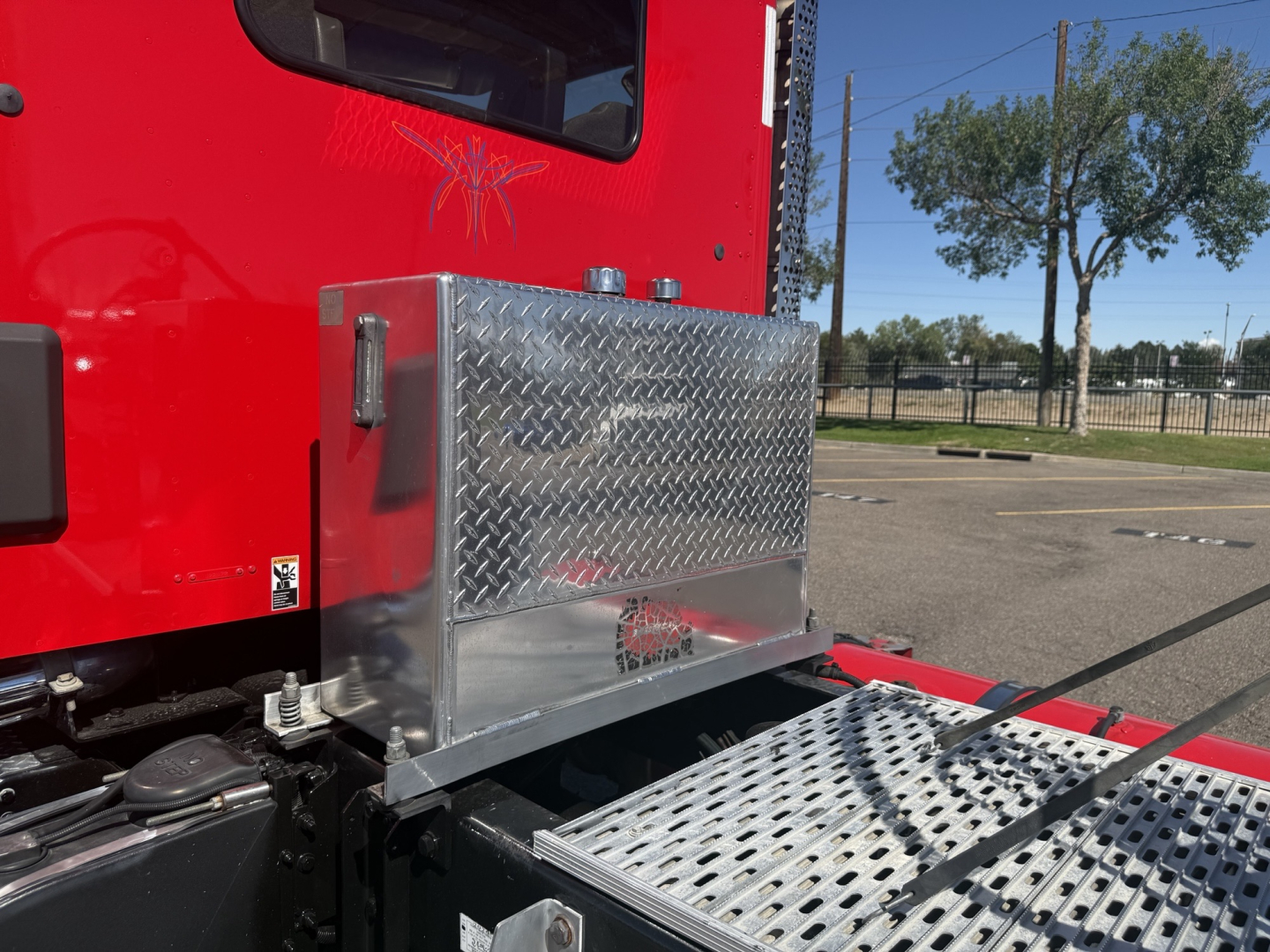 Aluminum toolbox mounted on the side of a red Kenworth T880 cab with diamond plate steps and side panel.