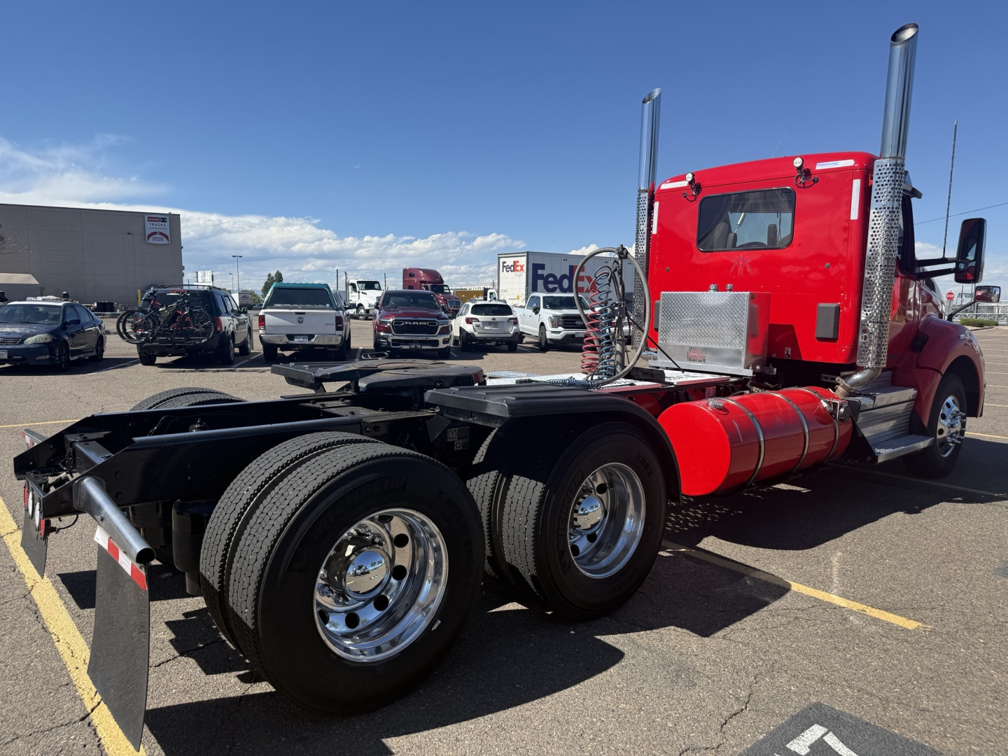 Kenworth T880 tractor chassis with red cab, dual rear axles, chrome wheels, and exposed fuel tank; visible text on cylinders and equipment.