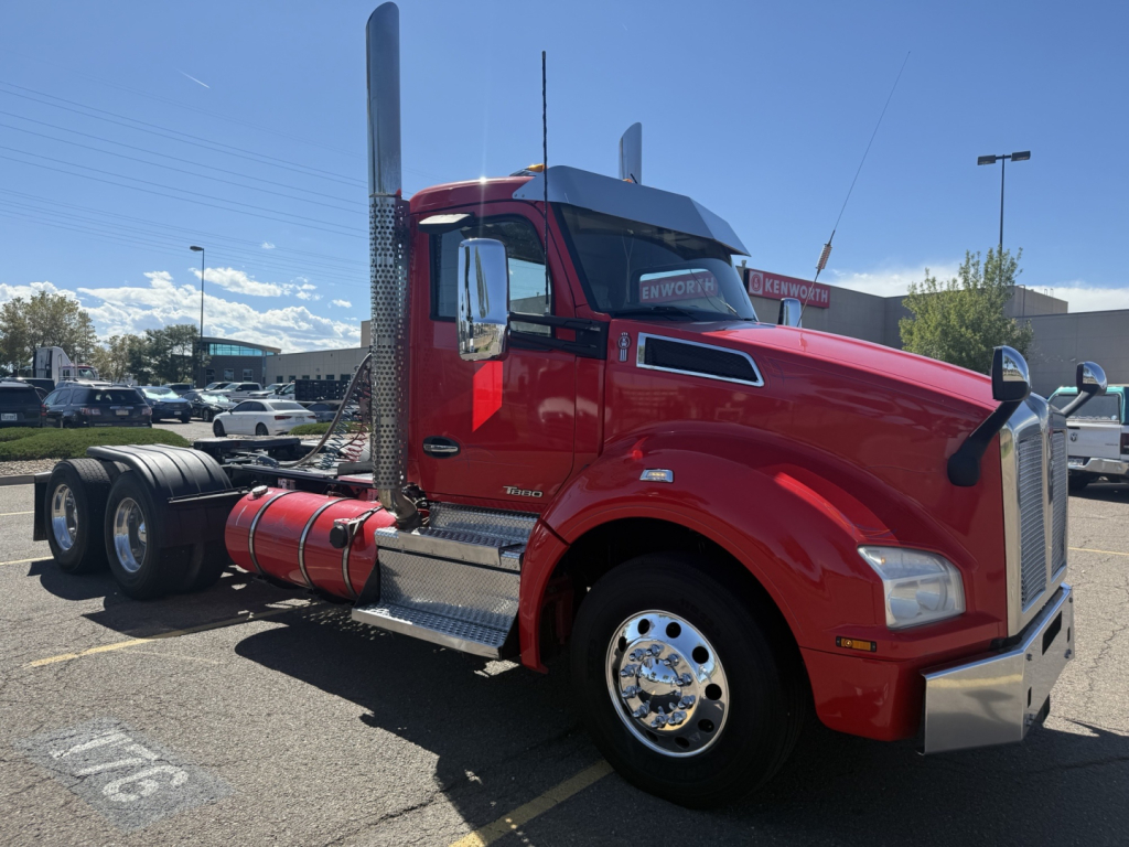 Kenworth T880 conventional daycab truck in red, side view showing chrome exhaust stack, air intake, fuel tank, and front bumper.