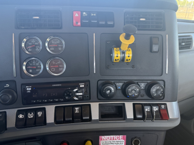 Kenworth T880 dash panel showing gauges, controls, and yellow gear shift lock in-cab with various switches and a radio.