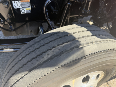 Kenworth T880 left front wheel well and engine bay with visible tire tread and warning labels. Text on label includes caution symbols and small text panels.