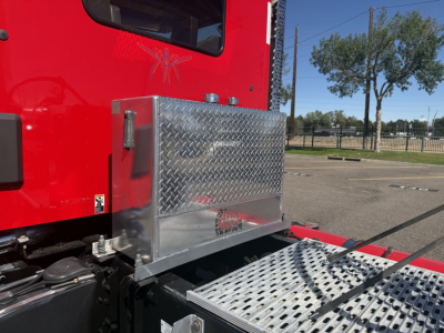 Aluminum toolbox mounted on the side of a red Kenworth T880 cab with diamond plate steps and side panel.