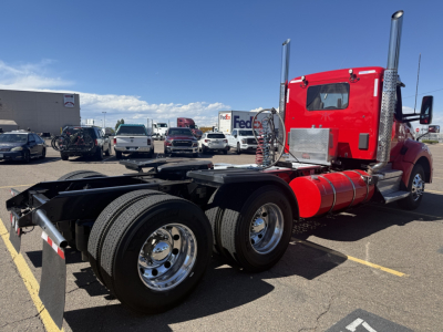 Kenworth T880 tractor chassis with red cab, dual rear axles, chrome wheels, and exposed fuel tank; visible text on cylinders and equipment.