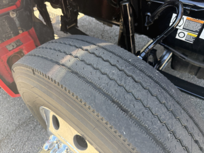 Kenworth T880 wheel and front tire visible in a daytime truck cab area; tread pattern and sidewall details; part of chassis and warning sticker in background.