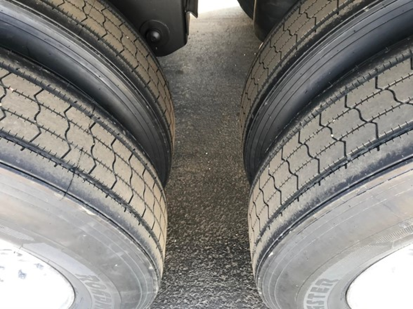Trailer tires visible from a close-up between dual axles, tread pattern and sidewalls in view.