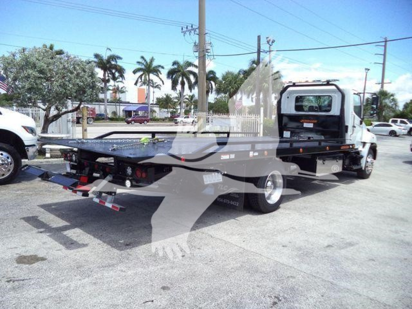 Flatbed tow truck with rollback equipment attached, rear view showing loading ramps and hydraulic system.