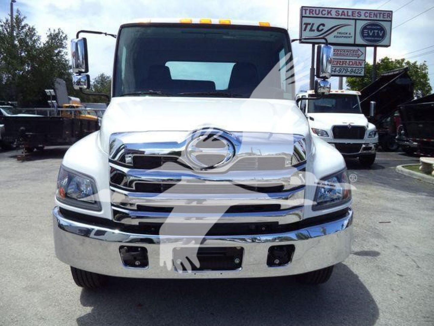 Front view of a white 2027 Hino L6 truck parked at a dealership lot, with chrome grille and bumper, side mirrors, and factory lights visible.