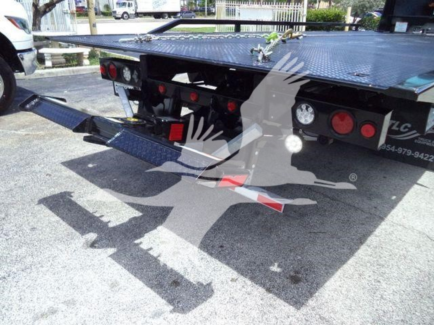 Rear view of a flatbed rollback truck showing loading ramps and taillights.