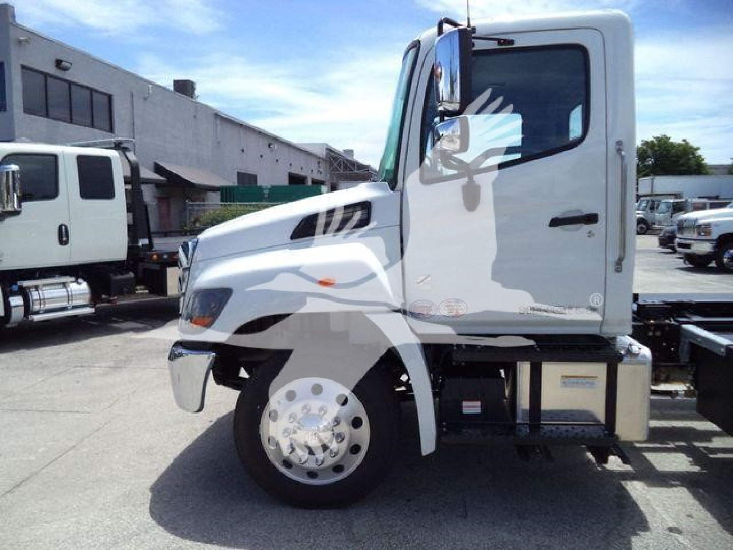 Truck cab side view of a 2027 Hino L6 rollback truck with white exterior and chrome wheel, stock number J50691FM.