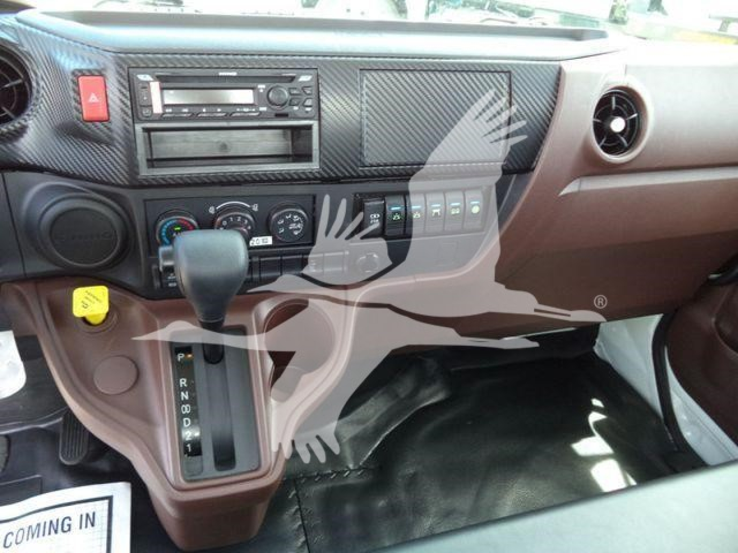 Dashboard and center console of a Hino L6 truck showing gear selector, climate controls, radio, and various switches.
