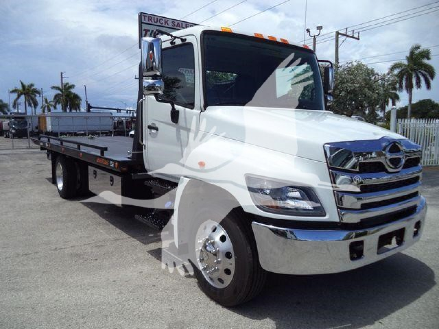 Truck cab and flatbed rollback body in white with chrome grille and side mirrors visible.