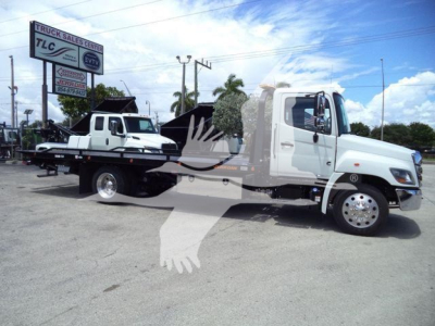 White 2027 Hino L6 rollback truck on lot with other vehicles in background.