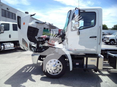 Front left-side view of a white 2027 Hino L6 rollback truck with cab tilted and engine visible, large front wheel, chrome hub, and open hood.