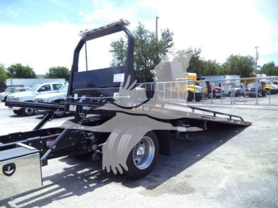 Truck bed with a ramp/wheel-lift setup on a rollback-style Hino chassis, side view showing flatbed and rear wheel, dealership lot in background.