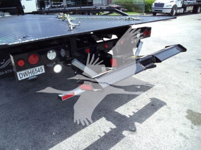 Flatbed of a rollback truck showing rear taillights, license plate DWH6545, and a lowered dual-retractable ramp with hydraulic mechanism.