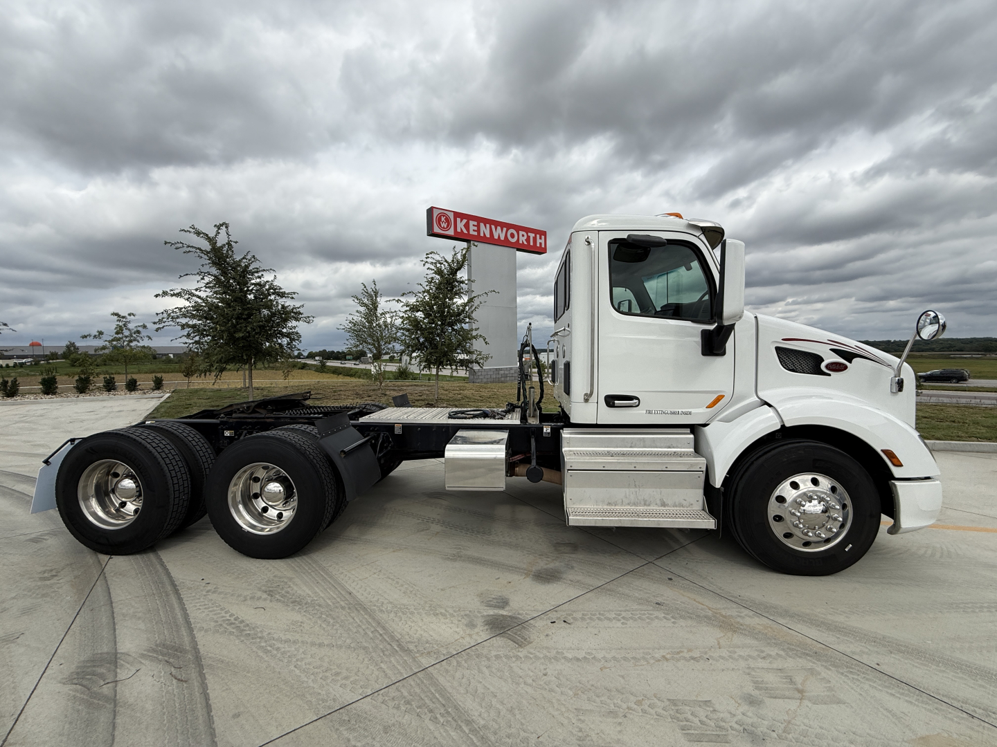 Peterbilt 579 tractor cab side view showing chassis and rear axles with stock number 0632204 on sign in background.