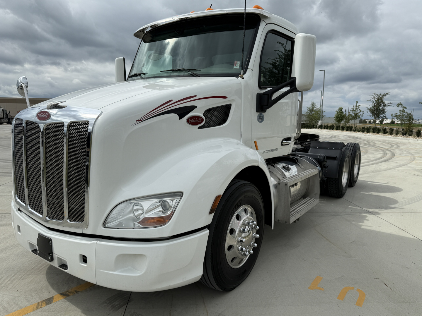 Peterbilt 579 conventional daycab truck in white, front left angle, with large grille, dual rear axles, and chrome wheels; VIN tag and stock number not visible in text on image.