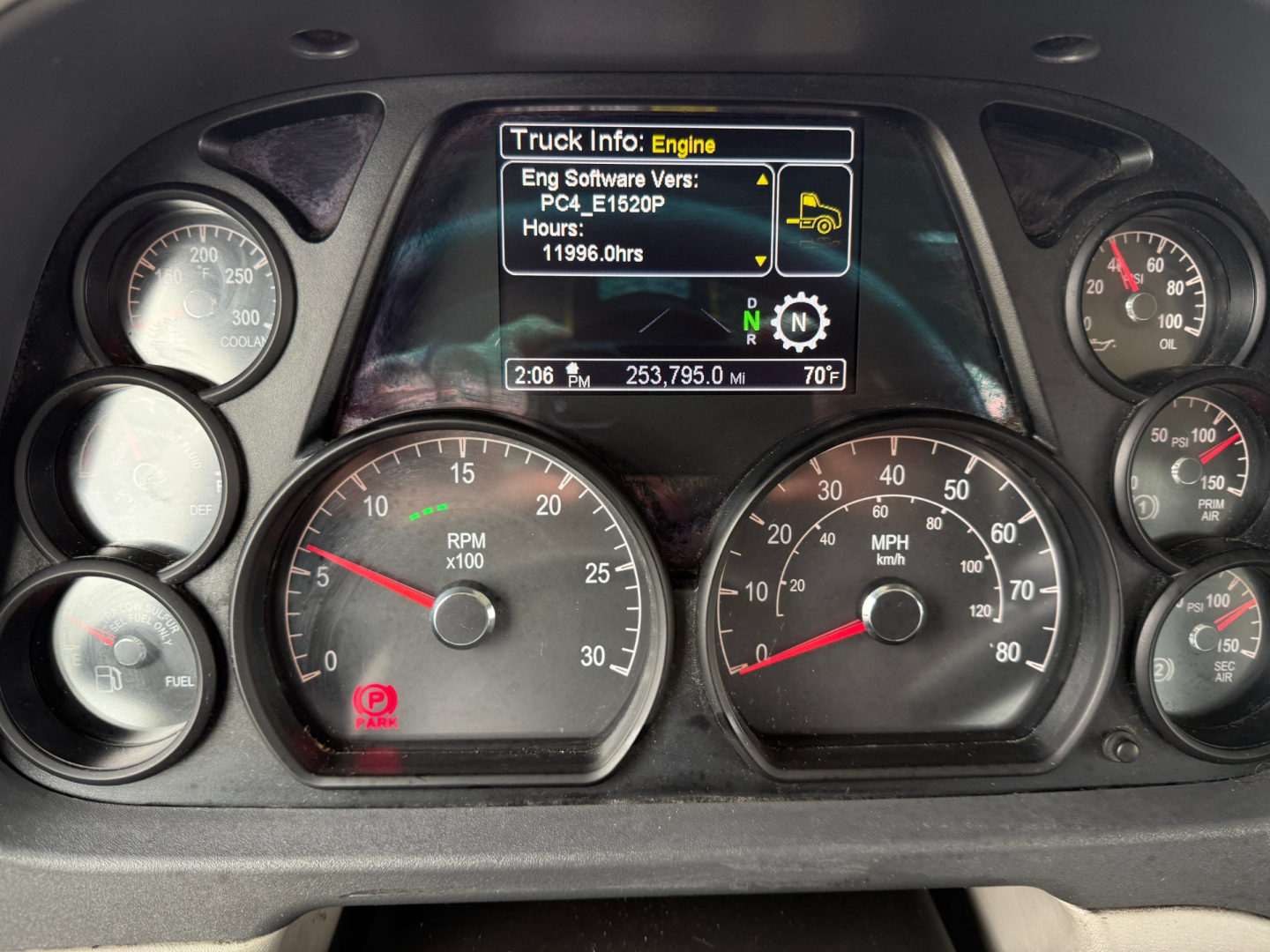 Peterbilt dashboard with multiple gauges and a central digital display showing engine information, hours and a small icon, surrounded by speedometer and tachometer dials.