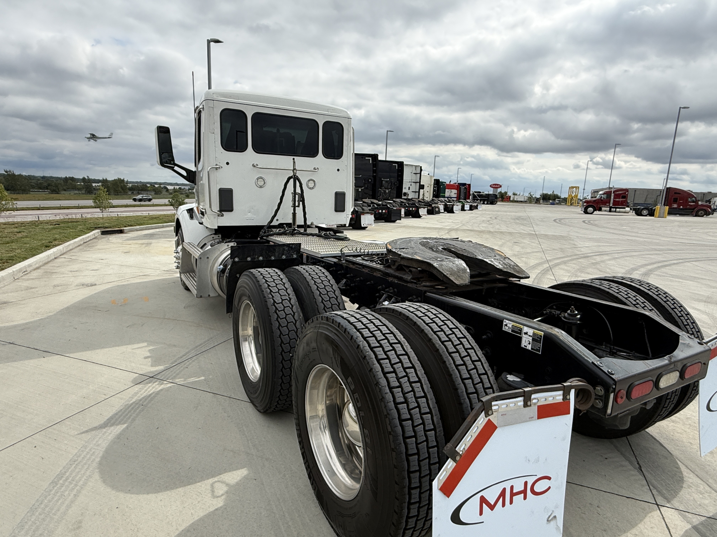 Peterbilt 579 tractor truck chassis rear view showing dual rear axles and fifth wheel, with white cab and mudflaps marked MHC.