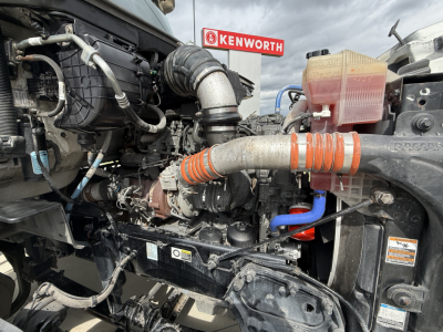 Peterbilt 579 engine bay showing air intake tube, coolant reservoir, hoses, and engine components in view.