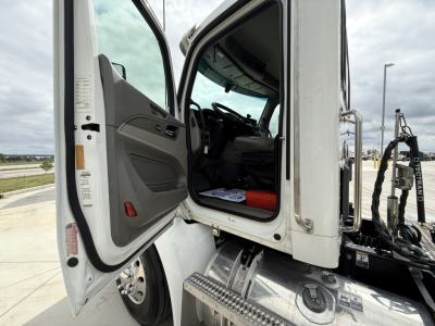 Peterbilt 579 truck cab interior with open door; dashboard and steering wheel visible; steps and chassis near doorway; some labels on door frame.