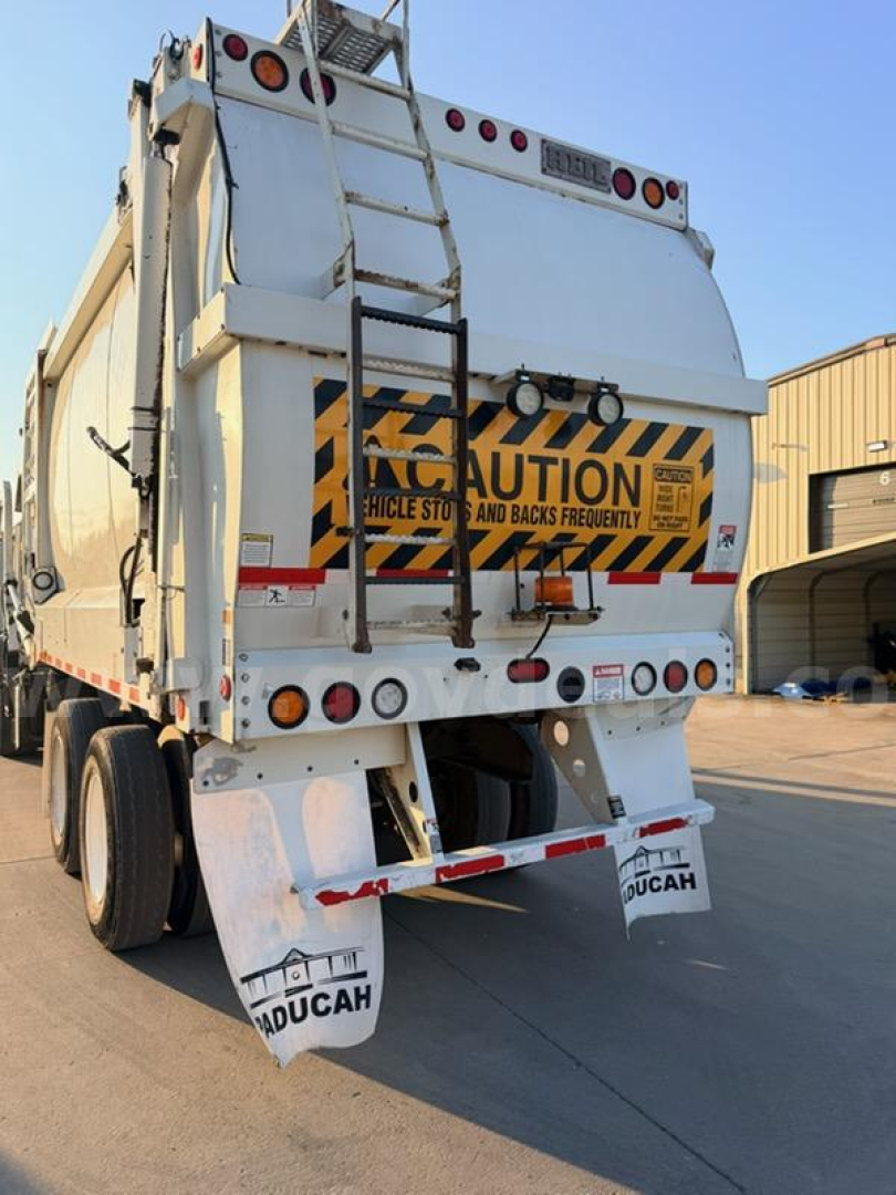 Rear view of a 2018 Mack MRU613 garbage truck showing hazard warning sticker, rear bumper, taillights, and mud flaps with AdUCAH branding.