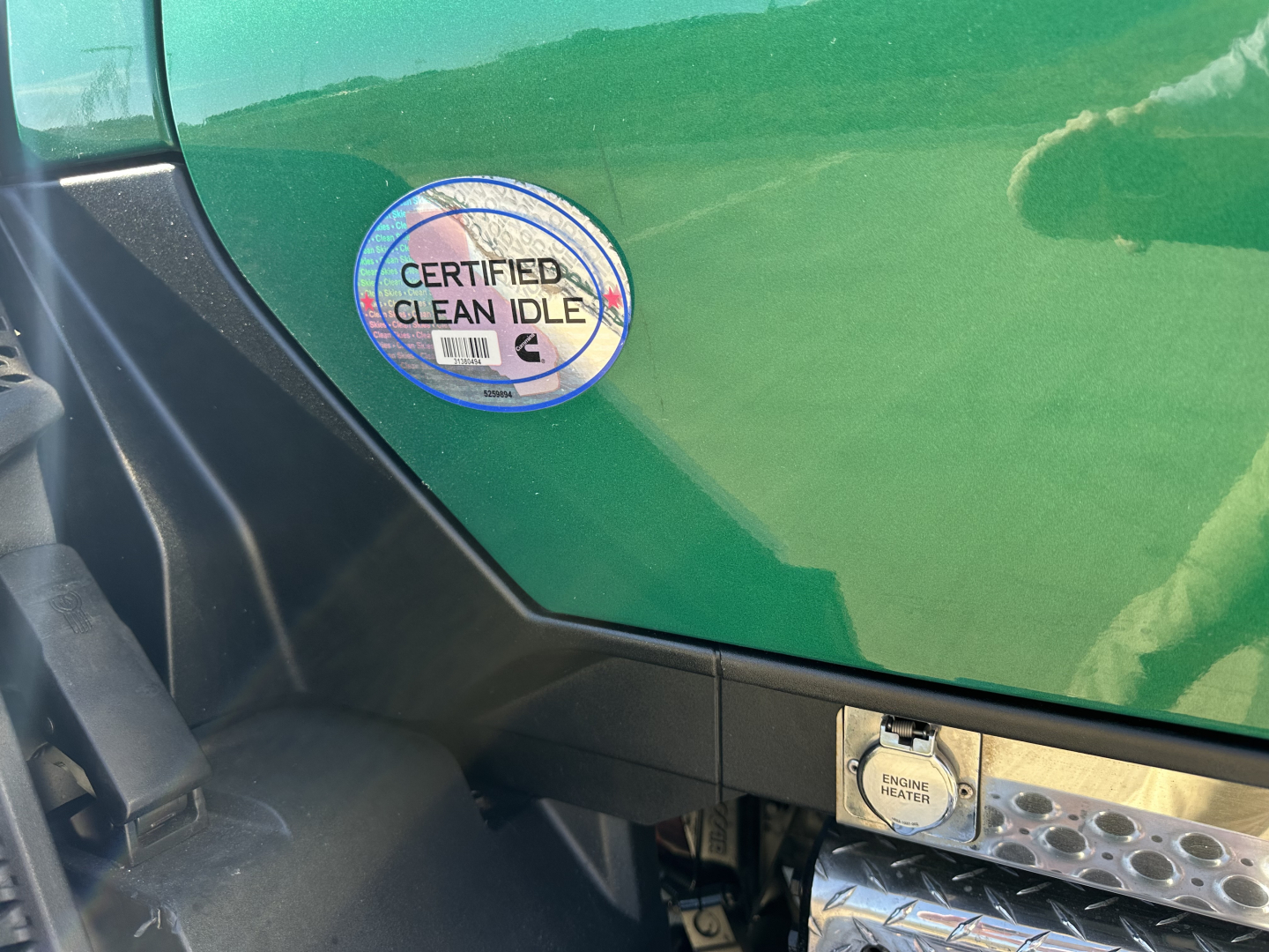 Kenworth T680 cab with green paint showing Certified Clean Idle badge on door panel and engine access button location.
