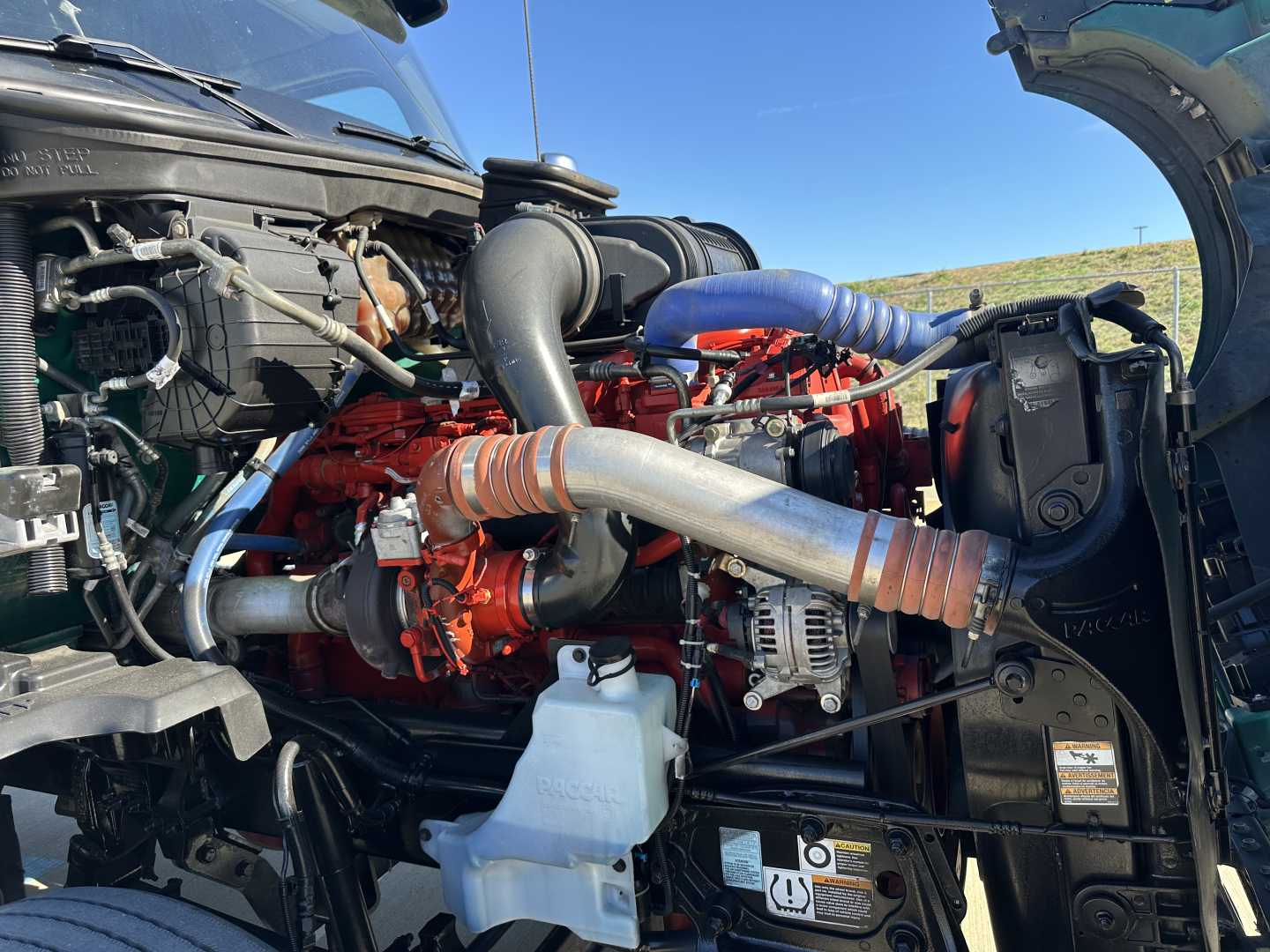 Kenworth T680 engine bay showing red diesel engine with orange piping and black hoses under open hood.