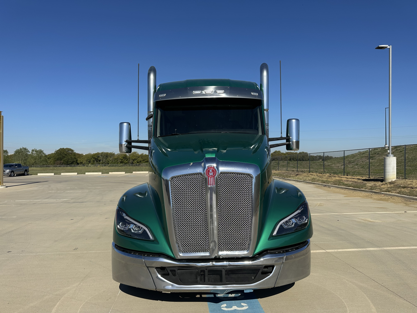 Kenworth T680 truck front view showing large chrome grille and green cab in a parking lot.