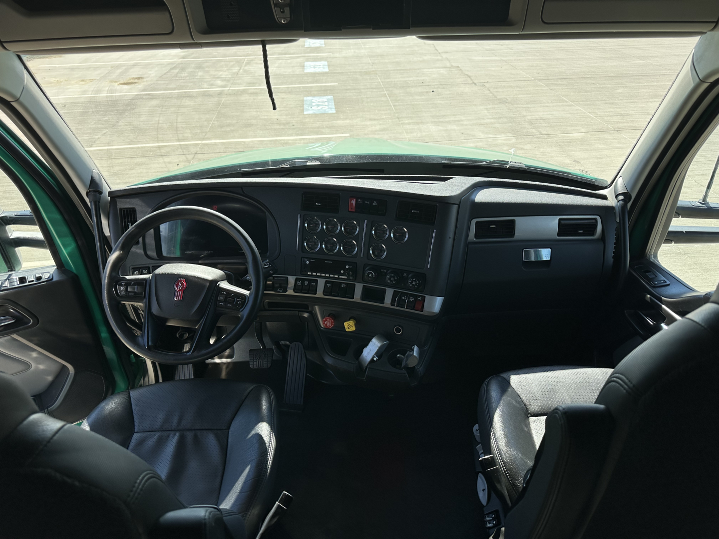 Truck cab interior showing steering wheel, dashboard, and driver seat from Kenworth T680; visible gauges and controls on the center stack.