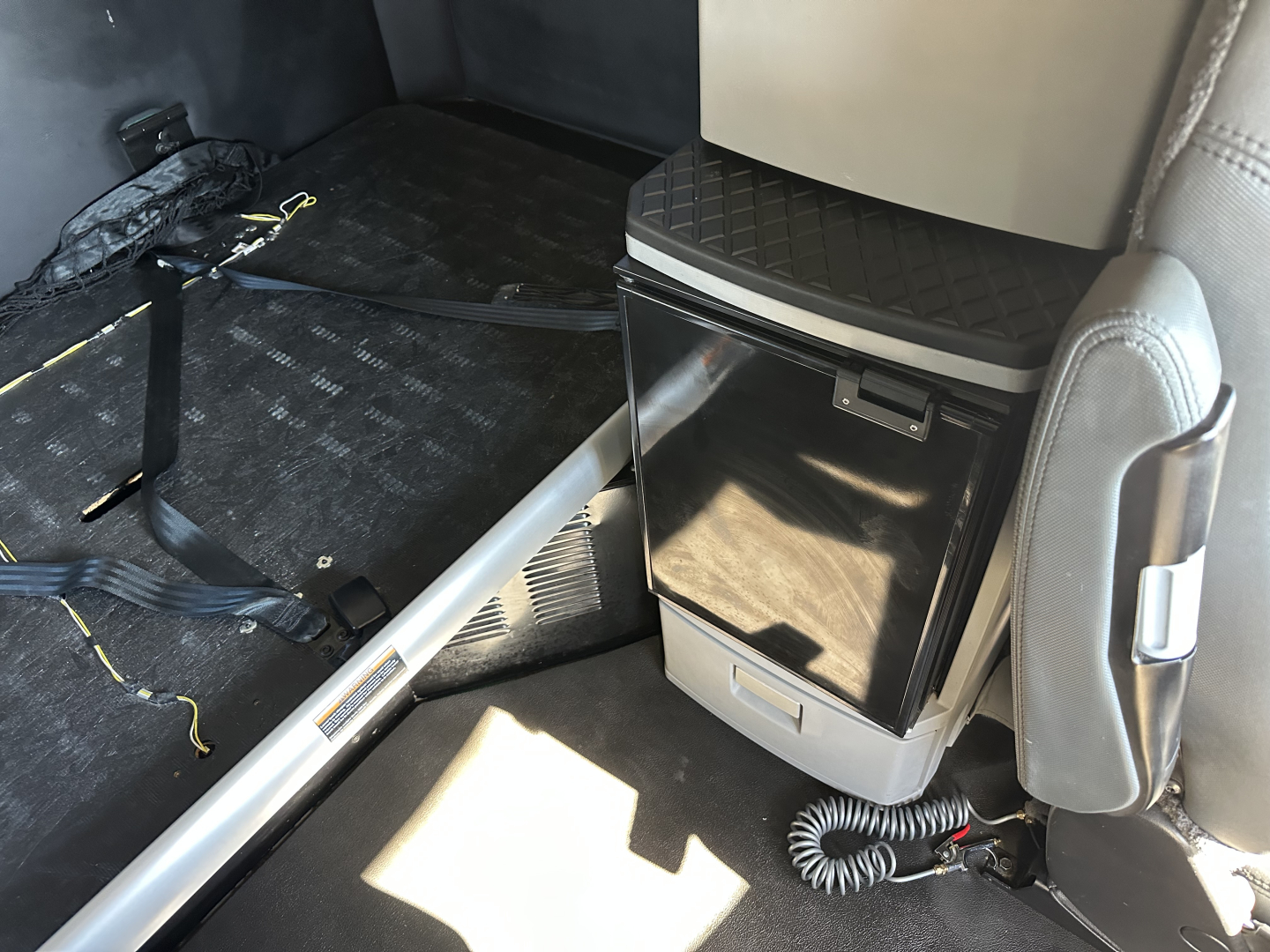 Kenworth T680 interior cab area showing storage fridge or cooler unit and seat base with floor mat.
