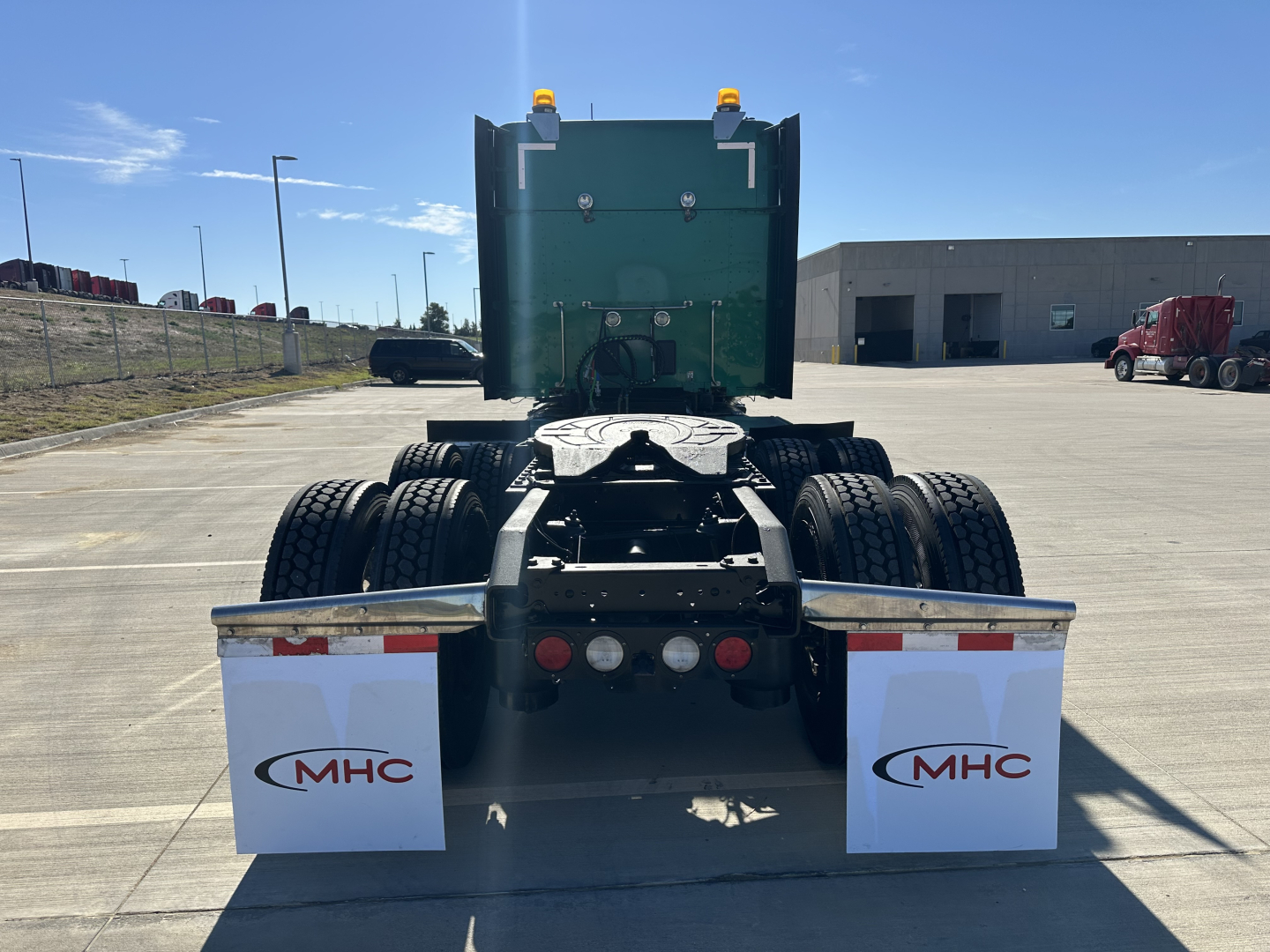 Back view of a Kenworth T680 tractor showing dual rear axles and MHC mud flaps with MHC logo.