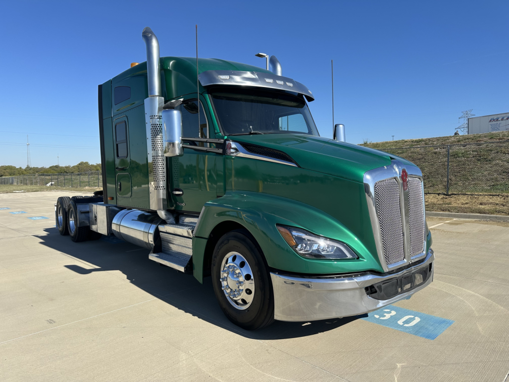 Kenworth T680 tractor in green showing chrome grille, exhaust stacks, side fuel tanks, and front wheel; no visible text readable on the truck from this angle.