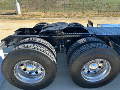 Kenworth truck rear wheels with dual tires and chrome rims; visible fifth wheel coupling and trailer wiring area on a flatbed, no identifying text readable on components.