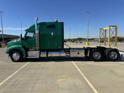Green Kenworth T680 tractor with a flatbed trailer in a parking lot, side view