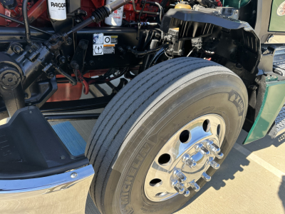 Kenworth T680 front wheel well and dual tires with chrome center hub, engine bay components visible, Michelin tire brand on tire sidewall.