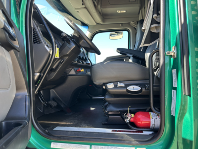 Kenworth T680 truck interior driver seat and dashboard view from open door showing steering wheel, ignition area, and fire extinguisher in cab.