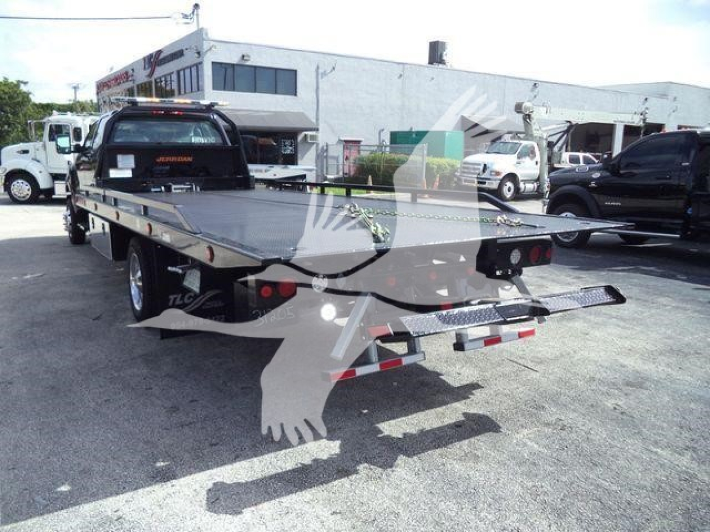 Flatbed tow truck trailer with extended bed and taillights in a dealership lot.