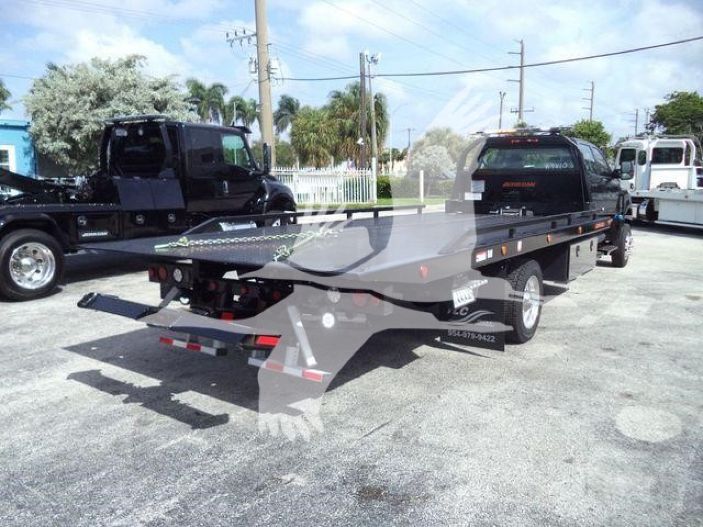 Flatbed tow truck trailer attached to a new International rollback truck with black and silver paint in a lot, showing rear lights and reflective tape.