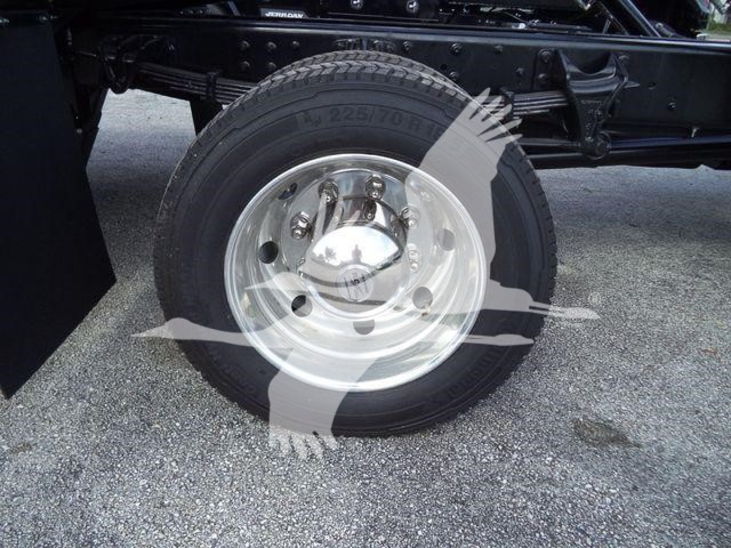 Truck wheel and suspension detail showing a front tire with steel rim and hubcap; partial undercarriage and frame visible.