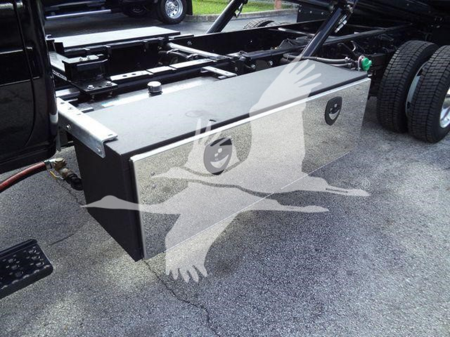 Flatbed truck chassis with a large rectangular metal toolbox mounted beside the cab; near wheels; no visible text on toolbox.