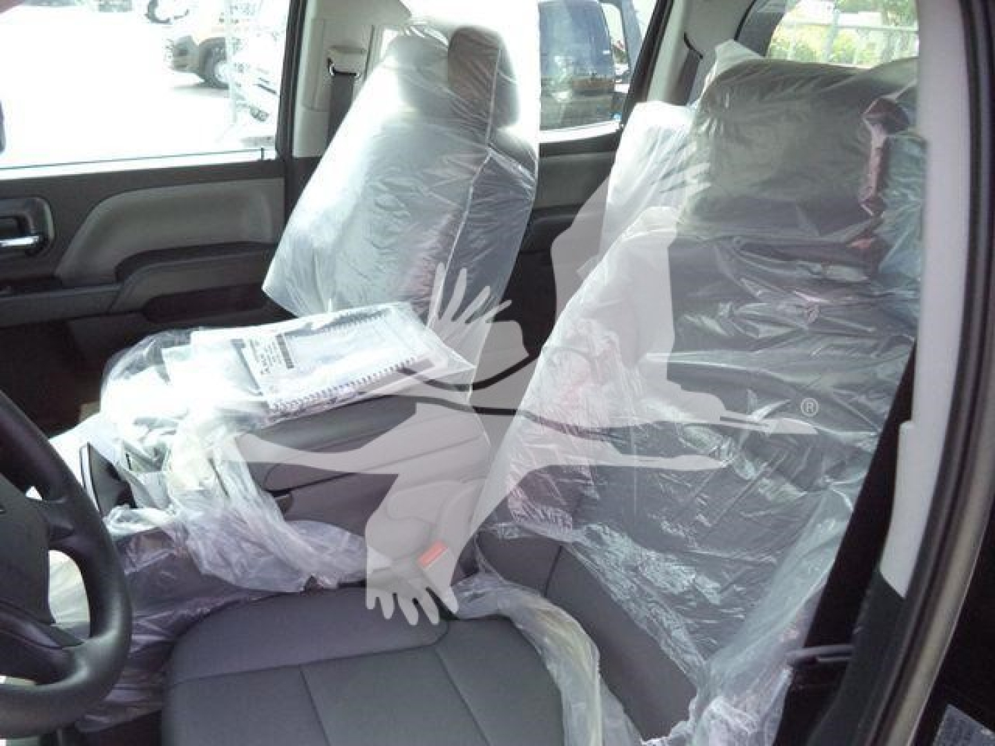 Truck cab interior with protective plastic on seats, steering wheel visible, light gray fabric upholstery, front seats wrapped in plastic.