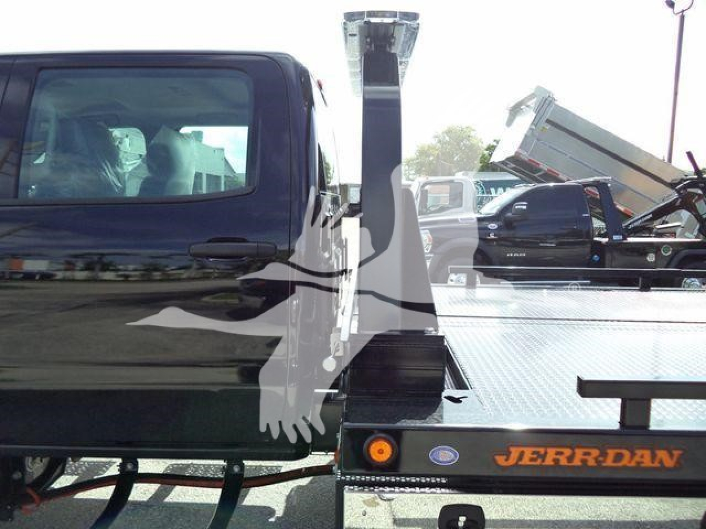 Flatbed tow truck with 'JERR-DAN' logo on deck and a black cab in the foreground; hydraulic tilt bed and elevated rear ramp visible.