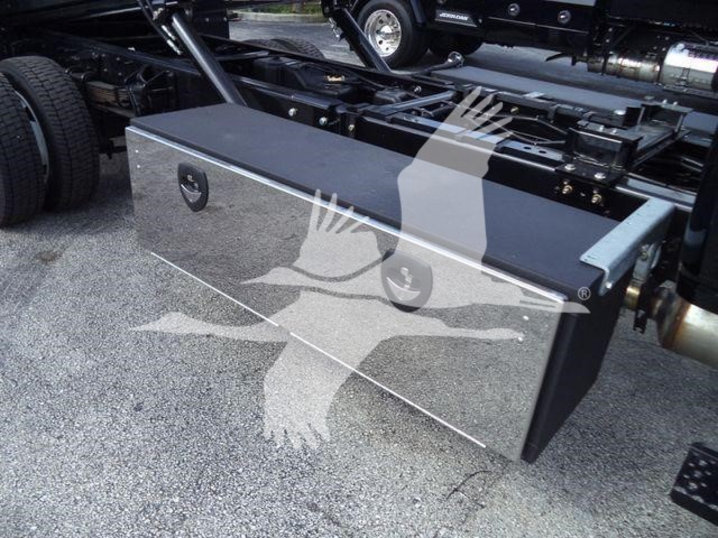 Aluminum toolbox mounted under truck chassis with latch handles and reflective surface; visible fuel/air line and frame components nearby.