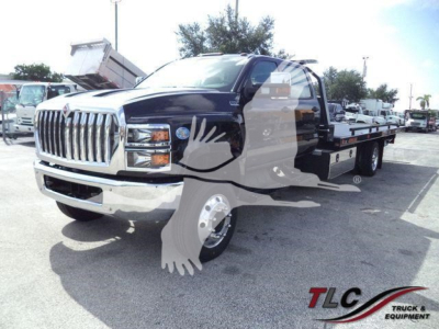 Flatbed tow truck with black cab and chrome front grille, International logo visible, watermark overlay of a white eagle, dealership lot in background.