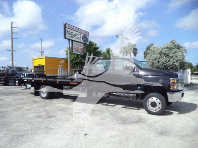 Truck in yard showing 2023 International CV rollback tow truck with flatbed and yellow equipment in background