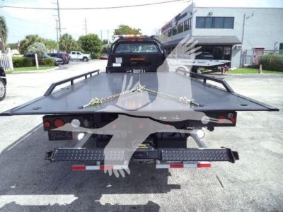 Flatbed tow truck bed on a trailer with wheel chocks and chains, rear view showing heavy-duty steel platform and taillights.