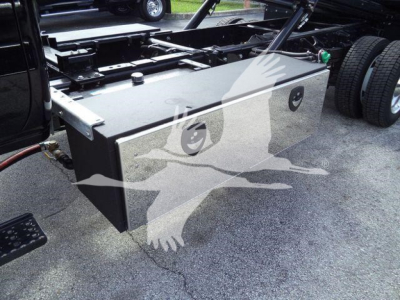 Flatbed truck chassis with a large rectangular metal toolbox mounted beside the cab; near wheels; no visible text on toolbox.